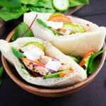 Pita stuffed with chicken, tomato, cucumber and spinach on wooden background