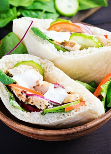Pita stuffed with chicken, tomato, cucumber and spinach on wooden background