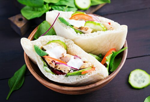 Pita stuffed with chicken, tomato, cucumber and spinach on wooden background