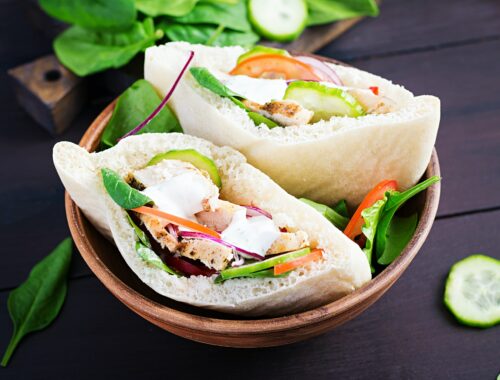 Pita stuffed with chicken, tomato, cucumber and spinach on wooden background