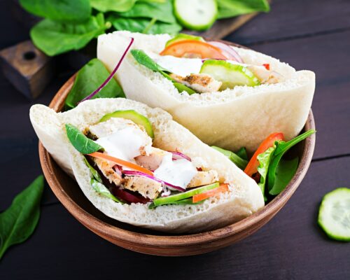 Pita stuffed with chicken, tomato, cucumber and spinach on wooden background