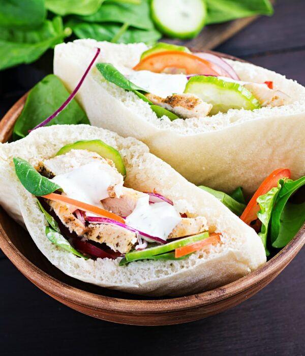 Pita stuffed with chicken, tomato, cucumber and spinach on wooden background