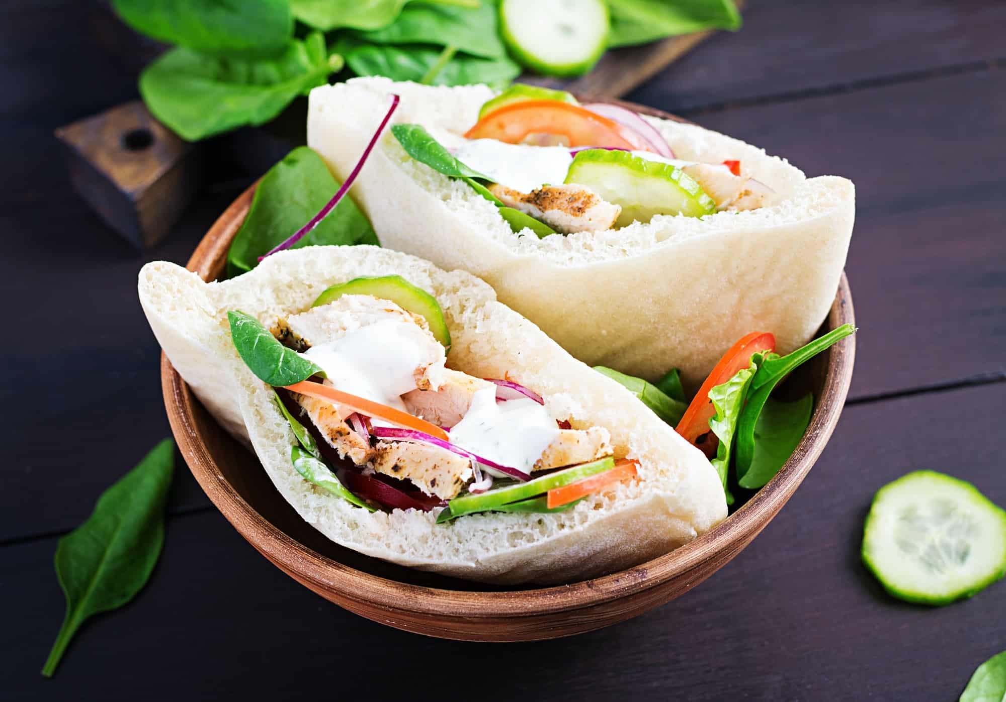 Pita stuffed with chicken, tomato, cucumber and spinach on wooden background