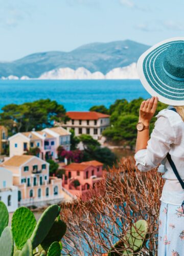Tourist female with blue sun hat and travel backpack enjoying greek vivid colored Assos town