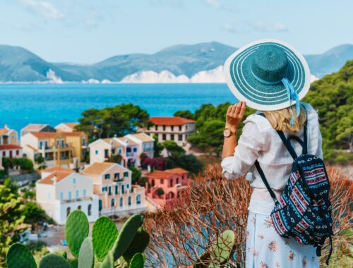 Tourist female with blue sun hat and travel backpack enjoying greek vivid colored Assos town