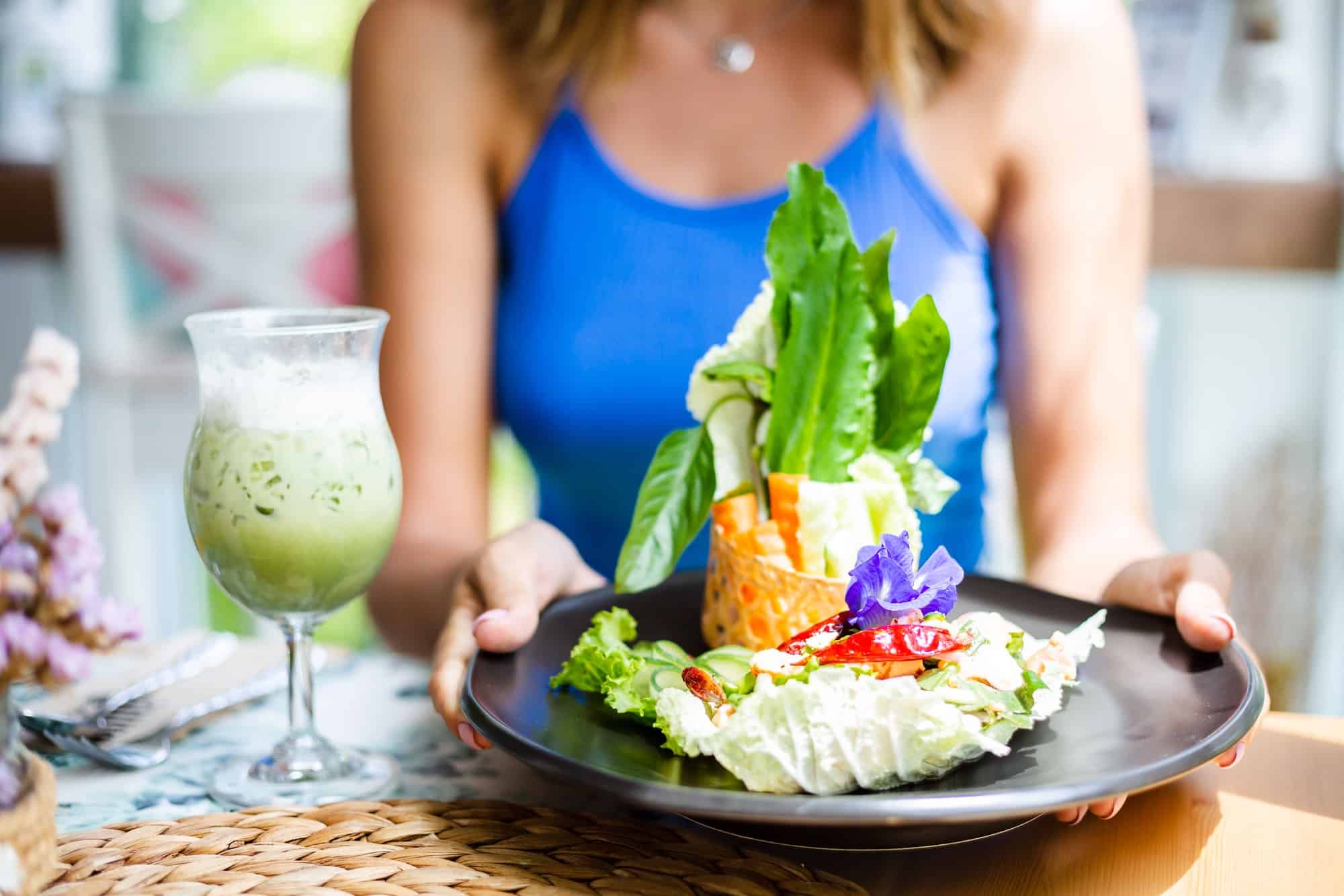 woman in cute blue top having spicy fresh salad with salmon and vegetables